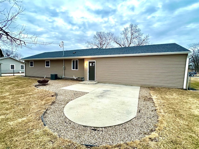 back of house featuring a lawn, a fire pit, a shingled roof, central AC unit, and a patio area