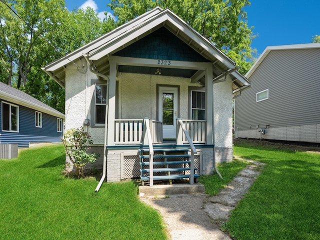 view of front of home with a front yard, covered porch, and stucco siding