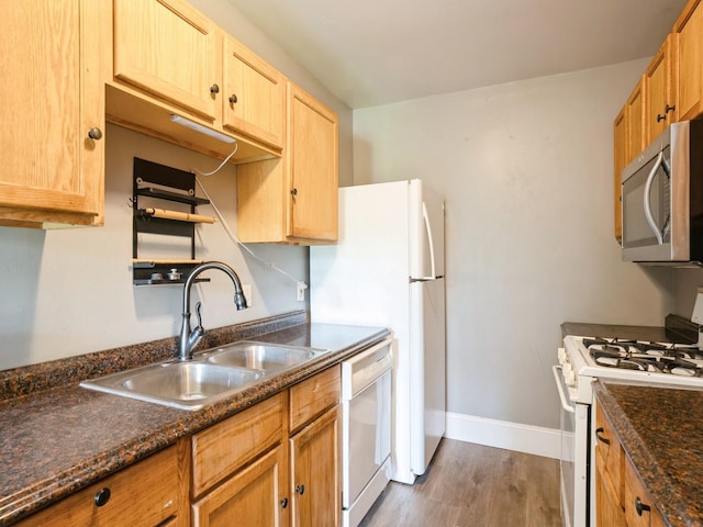 kitchen with a sink, dark stone counters, white appliances, baseboards, and dark wood-style flooring