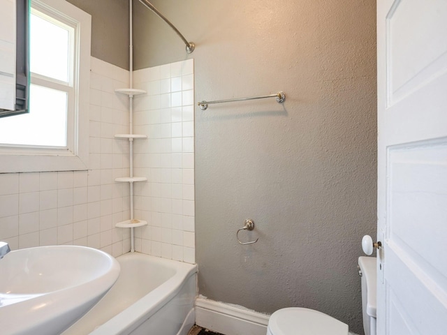 bathroom featuring a sink, toilet, shower / bath combination, and a textured wall