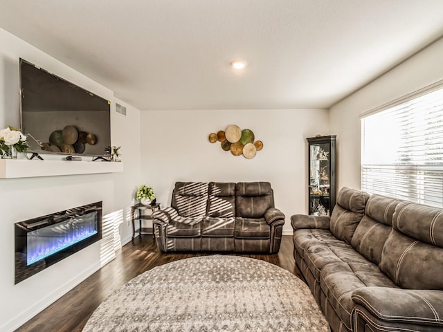 living area with a glass covered fireplace, dark wood-style floors, visible vents, and baseboards