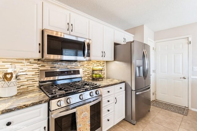 kitchen featuring dark stone counters, light tile patterned flooring, decorative backsplash, white cabinets, and appliances with stainless steel finishes