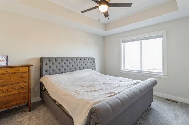 bedroom featuring carpet flooring, a tray ceiling, baseboards, and a ceiling fan