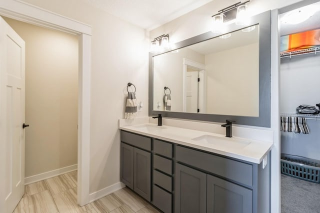 full bathroom with double vanity, a spacious closet, and baseboards