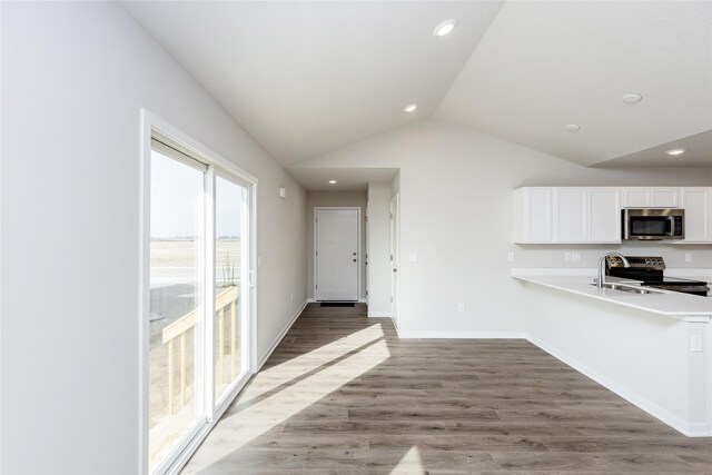 kitchen featuring wood finished floors, stainless steel appliances, white cabinets, light countertops, and vaulted ceiling