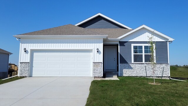 view of front of property featuring a shingled roof, concrete driveway, a front yard, a garage, and stone siding