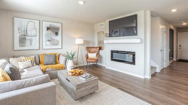 living room featuring a glass covered fireplace, recessed lighting, baseboards, and wood finished floors