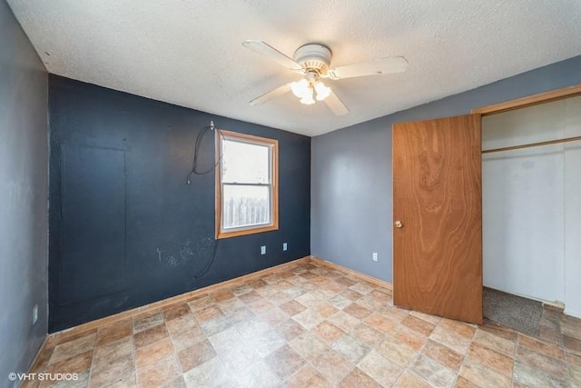 unfurnished bedroom featuring baseboards, ceiling fan, a closet, stone finish floor, and a textured ceiling