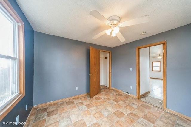 spare room featuring visible vents, baseboards, ceiling fan, stone finish floor, and a textured ceiling