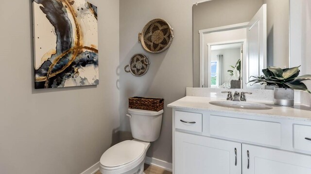 half bath featuring baseboards, toilet, and vanity