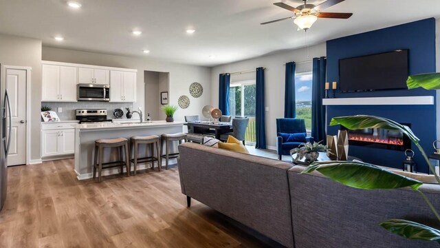 living room featuring light wood-style flooring, a ceiling fan, a glass covered fireplace, recessed lighting, and baseboards
