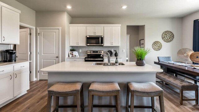 kitchen with decorative backsplash, appliances with stainless steel finishes, a kitchen breakfast bar, white cabinetry, and a sink