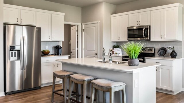 kitchen with a sink, stainless steel appliances, white cabinets, and a center island with sink