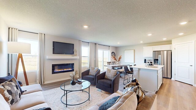 living room with light wood finished floors, a glass covered fireplace, recessed lighting, and a textured ceiling