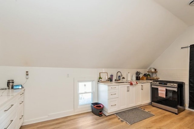 222 W State St, Colfax, IA 50054 - kitchen featuring stainless steel range with gas cooktop, light wood-style floors, light countertops, vaulted ceiling, and white cabinets