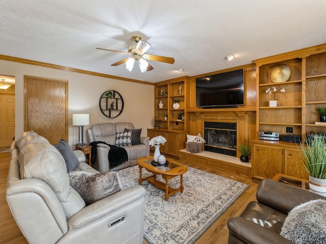 living area featuring ornamental molding, wood finished floors, a glass covered fireplace, a textured ceiling, and a ceiling fan