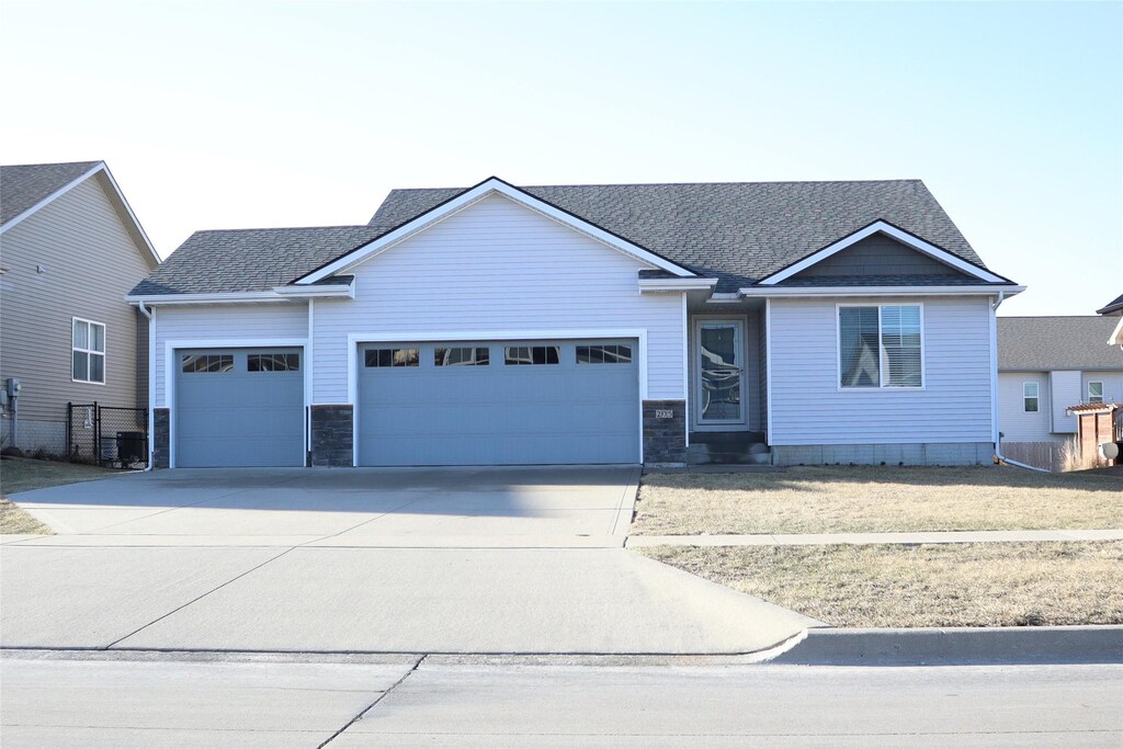 ranch-style home with stone siding, central AC, concrete driveway, a front yard, and an attached garage