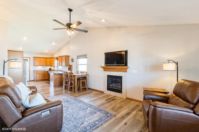living room featuring light wood-type flooring, a tiled fireplace, baseboards, ceiling fan, and vaulted ceiling