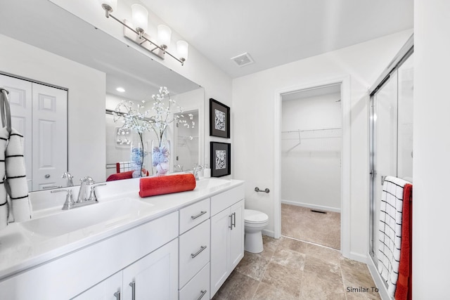 bathroom with a stall shower, double vanity, a walk in closet, toilet, and stone finish flooring