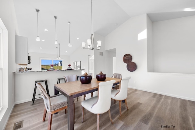 dining room with light wood finished floors, a chandelier, high vaulted ceiling, and baseboards