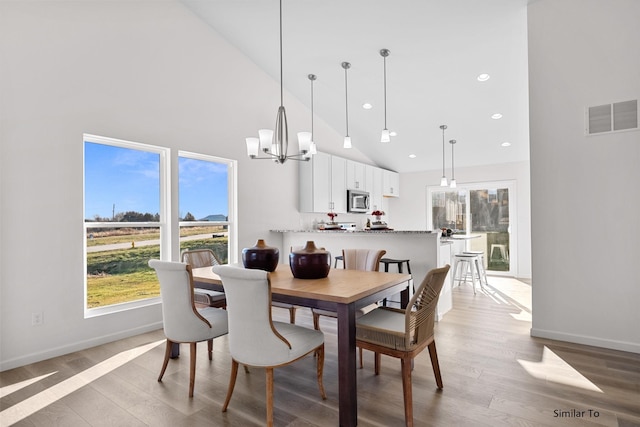 dining room featuring high vaulted ceiling, healthy amount of natural light, a chandelier, light wood-style floors, and baseboards