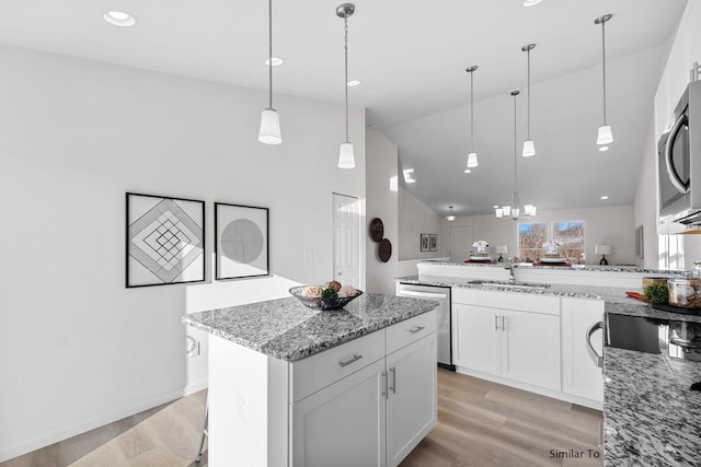 kitchen featuring appliances with stainless steel finishes, a sink, light stone counters, white cabinets, and a kitchen island