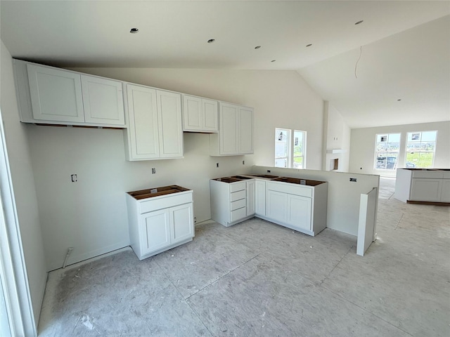 kitchen with vaulted ceiling, plenty of natural light, white cabinetry, and a peninsula