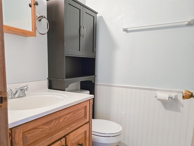 half bathroom with toilet, vanity, and wainscoting