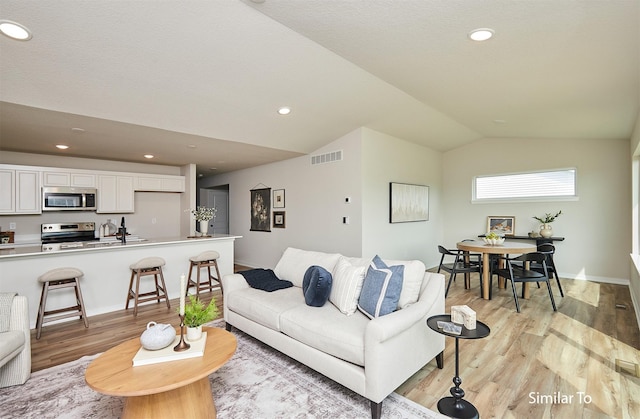 living room featuring lofted ceiling, visible vents, light wood finished floors, and baseboards