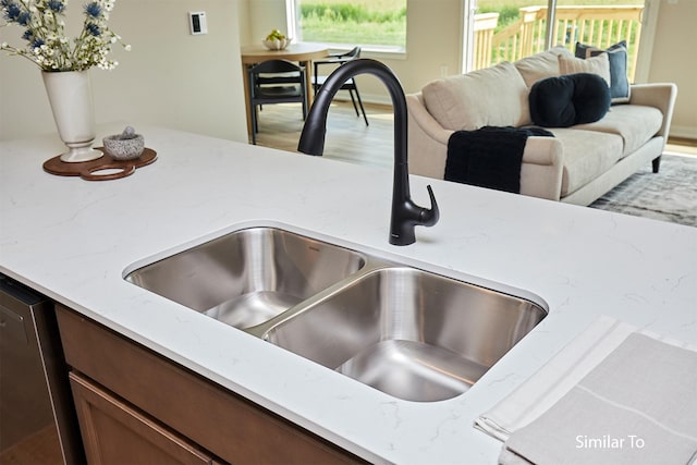 room details with dishwasher, light stone countertops, wood finished floors, and a sink