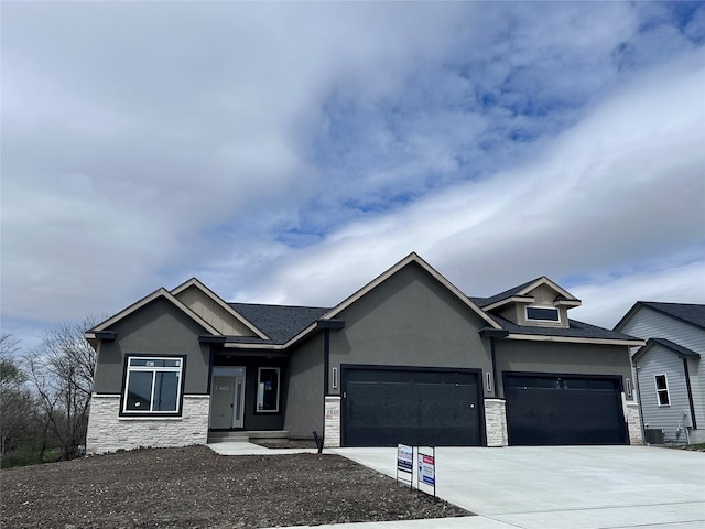 view of front of home featuring driveway, a garage, central AC, stone siding, and stucco siding