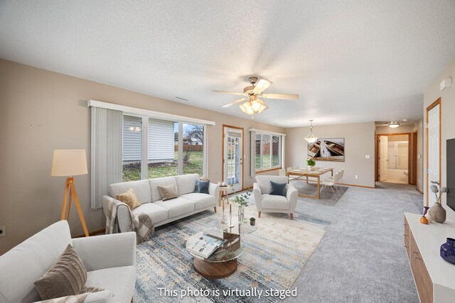 living area featuring a textured ceiling, baseboards, light colored carpet, and ceiling fan