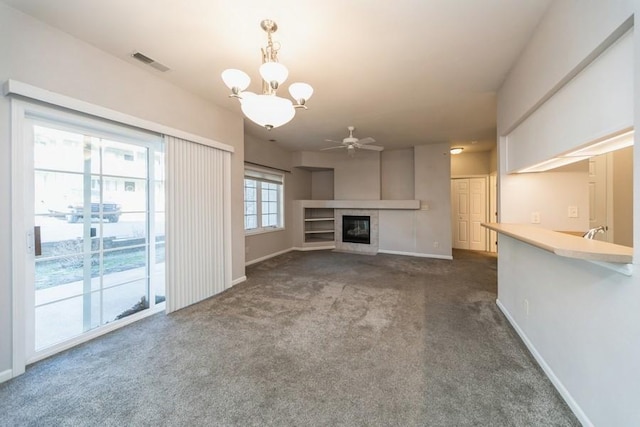 unfurnished living room featuring visible vents, baseboards, ceiling fan with notable chandelier, a glass covered fireplace, and dark colored carpet