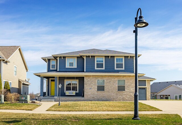 view of front of property with a front yard, stone siding, concrete driveway, a garage, and a porch