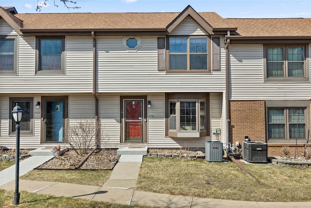 view of property with brick siding, central AC, roof with shingles, and a front lawn