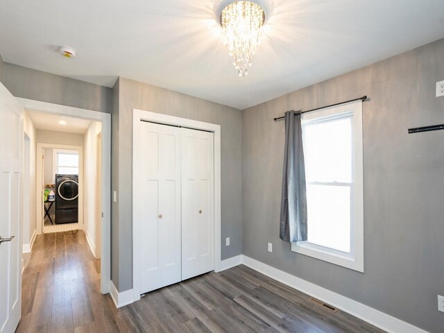 613 E 8th St N, Newton, IA 50208 - unfurnished bedroom featuring washer / dryer, a chandelier, dark wood-style flooring, baseboards, and a closet