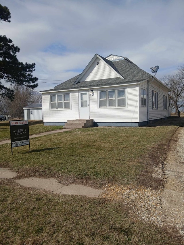 view of front of property featuring entry steps, a shingled roof, and a front lawn