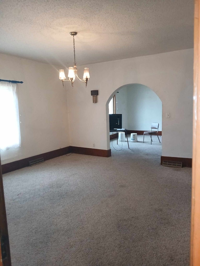 carpeted spare room with visible vents, baseboards, arched walkways, a chandelier, and a textured ceiling
