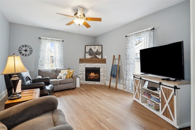 321 W Maple St, Roland, IA 50236 - living room featuring a stone fireplace, baseboards, light wood finished floors, and ceiling fan