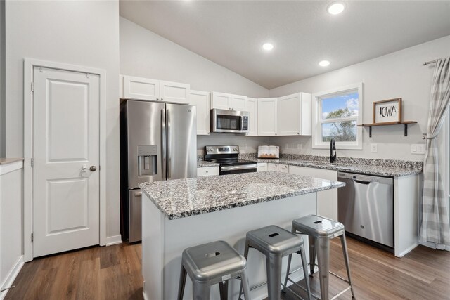 kitchen featuring a kitchen bar, vaulted ceiling, stainless steel appliances, a sink, and white cabinets