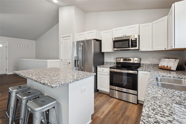 kitchen with lofted ceiling, white cabinetry, wood finished floors, and appliances with stainless steel finishes