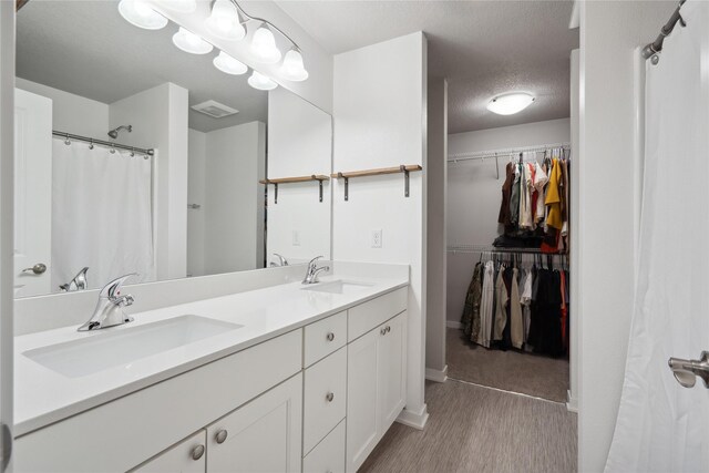 full bath featuring a walk in closet, visible vents, a sink, and a textured ceiling