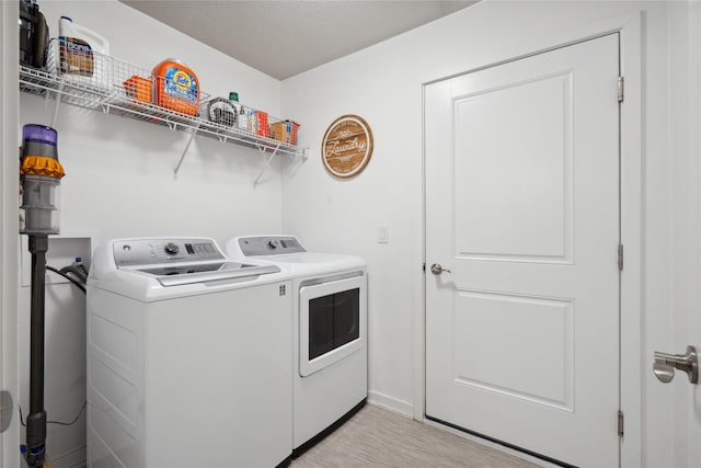 clothes washing area with light wood-type flooring, washing machine and clothes dryer, laundry area, and a textured ceiling