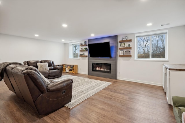 living room featuring light wood finished floors, baseboards, a fireplace, and recessed lighting