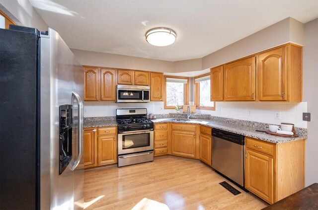15026 Hawthorn Dr, Clive, IA 50325 - kitchen featuring appliances with stainless steel finishes, a sink, light wood-style flooring, backsplash, and light stone countertops