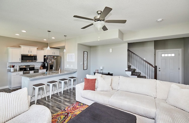 living room with stairs, ceiling fan, baseboards, dark wood-style flooring, and recessed lighting