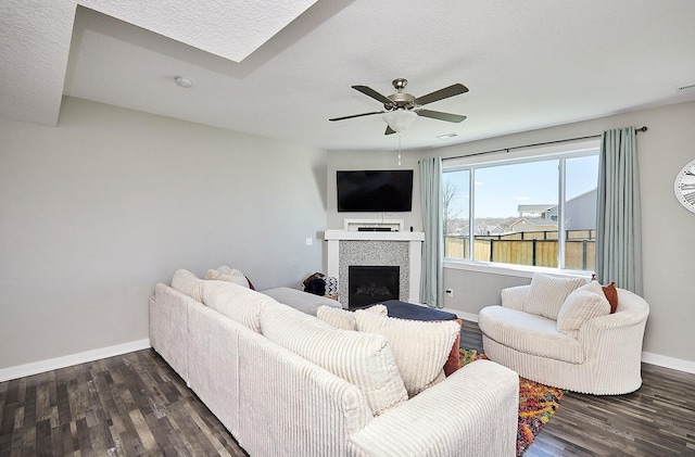 living room with ceiling fan, baseboards, dark wood-style flooring, and a tiled fireplace