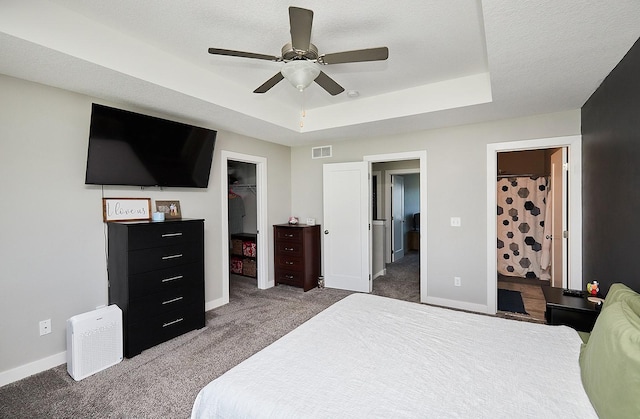 carpeted bedroom with a spacious closet, a tray ceiling, visible vents, a closet, and baseboards
