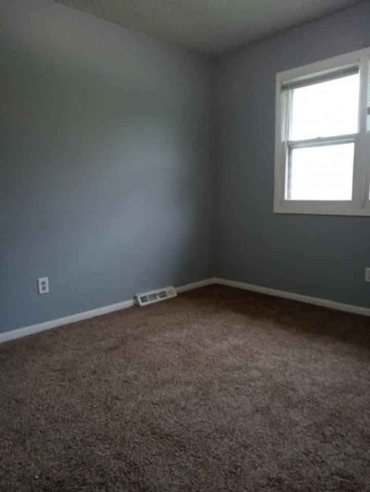 empty room with visible vents, dark carpet, and baseboards
