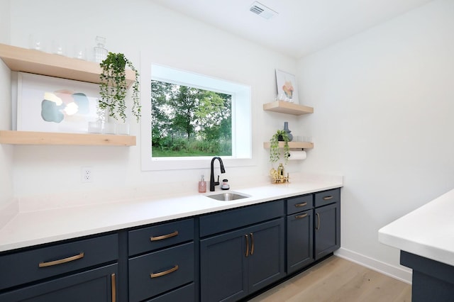 bar with baseboards, visible vents, a sink, and light wood finished floors